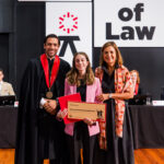 Três pessoas posando com um certificado em frente a faixa da NOVA School of Law