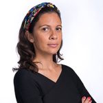 Uma mulher com um top preto de braços cruzados e uma bandana colorida no cabelo